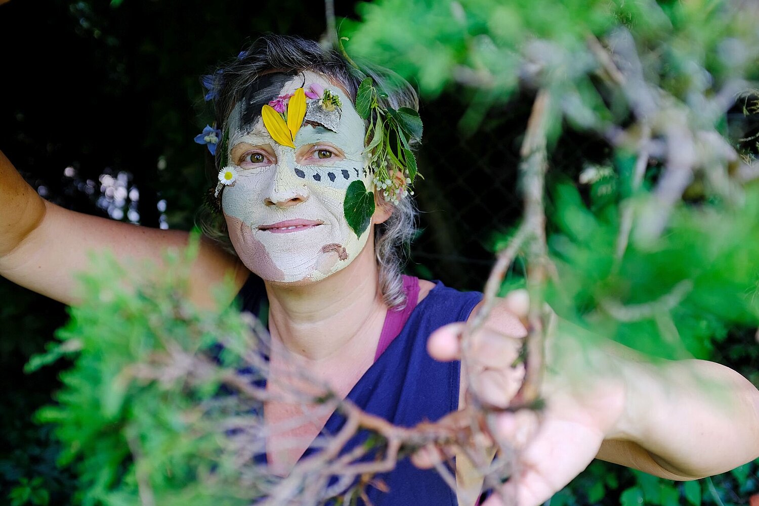 Frau mit bunt bemaltem Gesicht zwischen Blättern