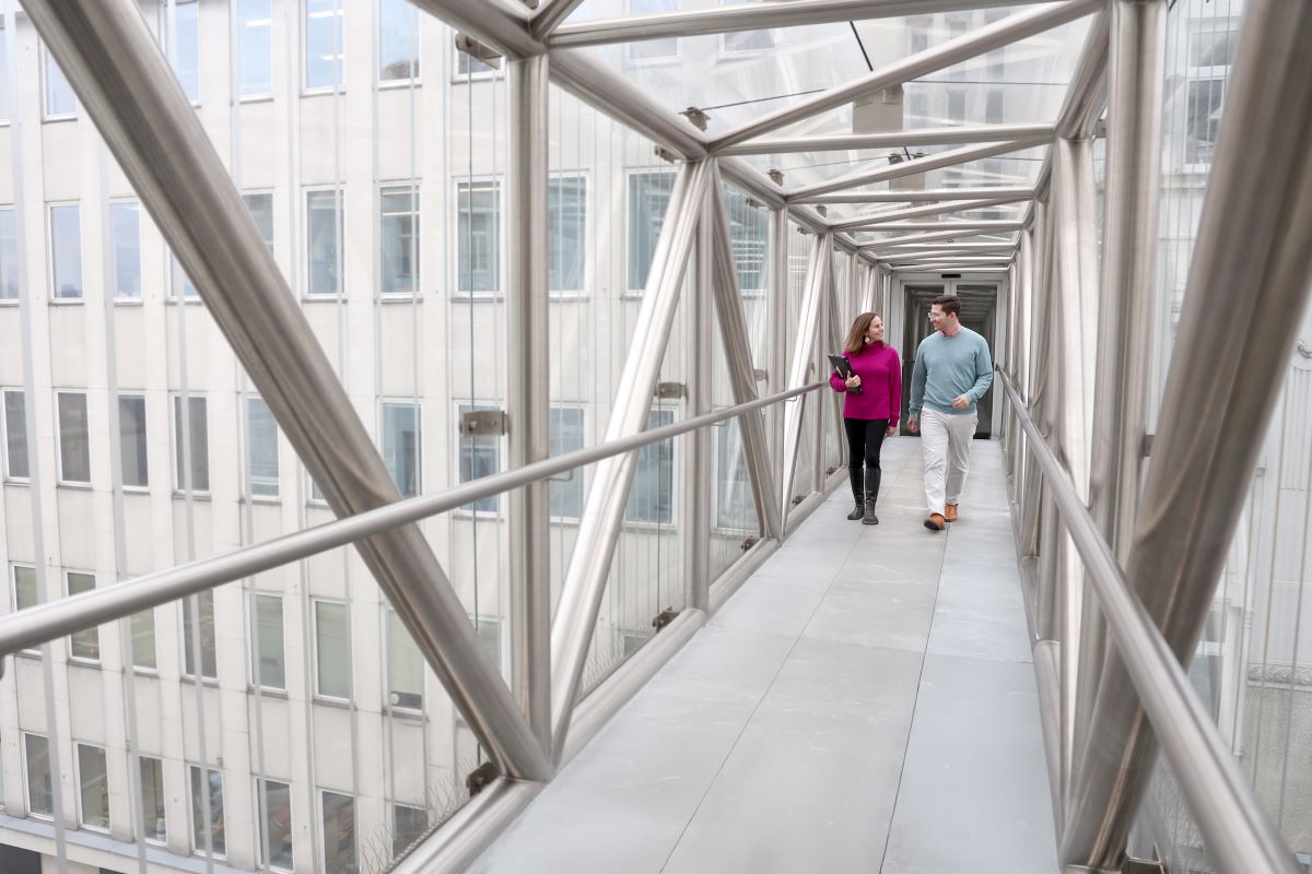 Zwei Personen gehen über eine geschlossene Brücke aus Glas.