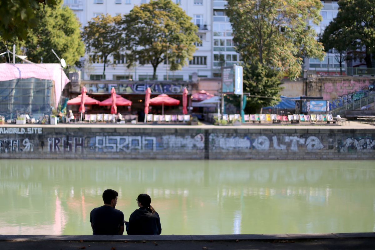 Zwei Personen sitzen am Donaukanal in Wien.