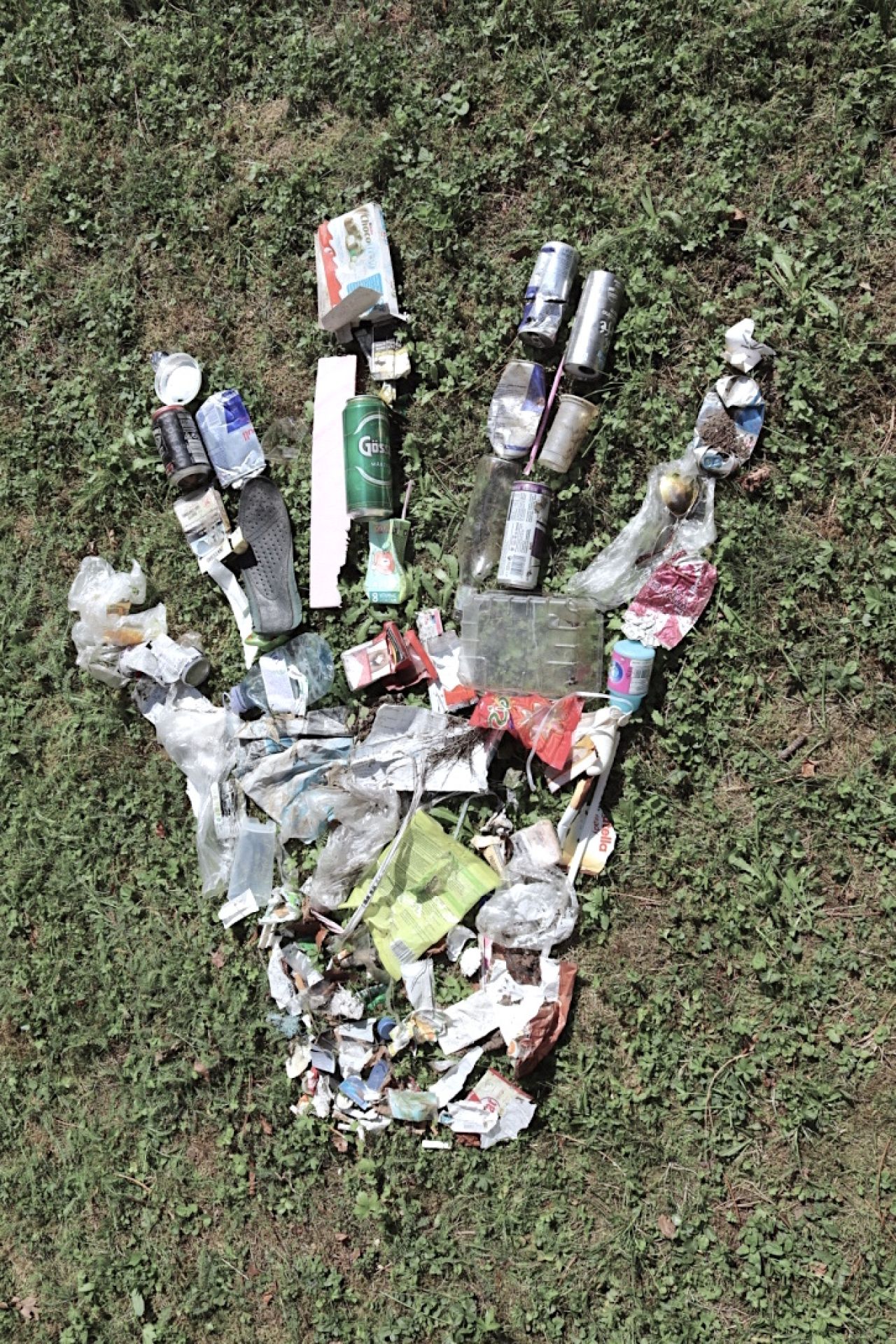 auf einer Wiese liegt eine Hand die aus Müll gestaltet ist